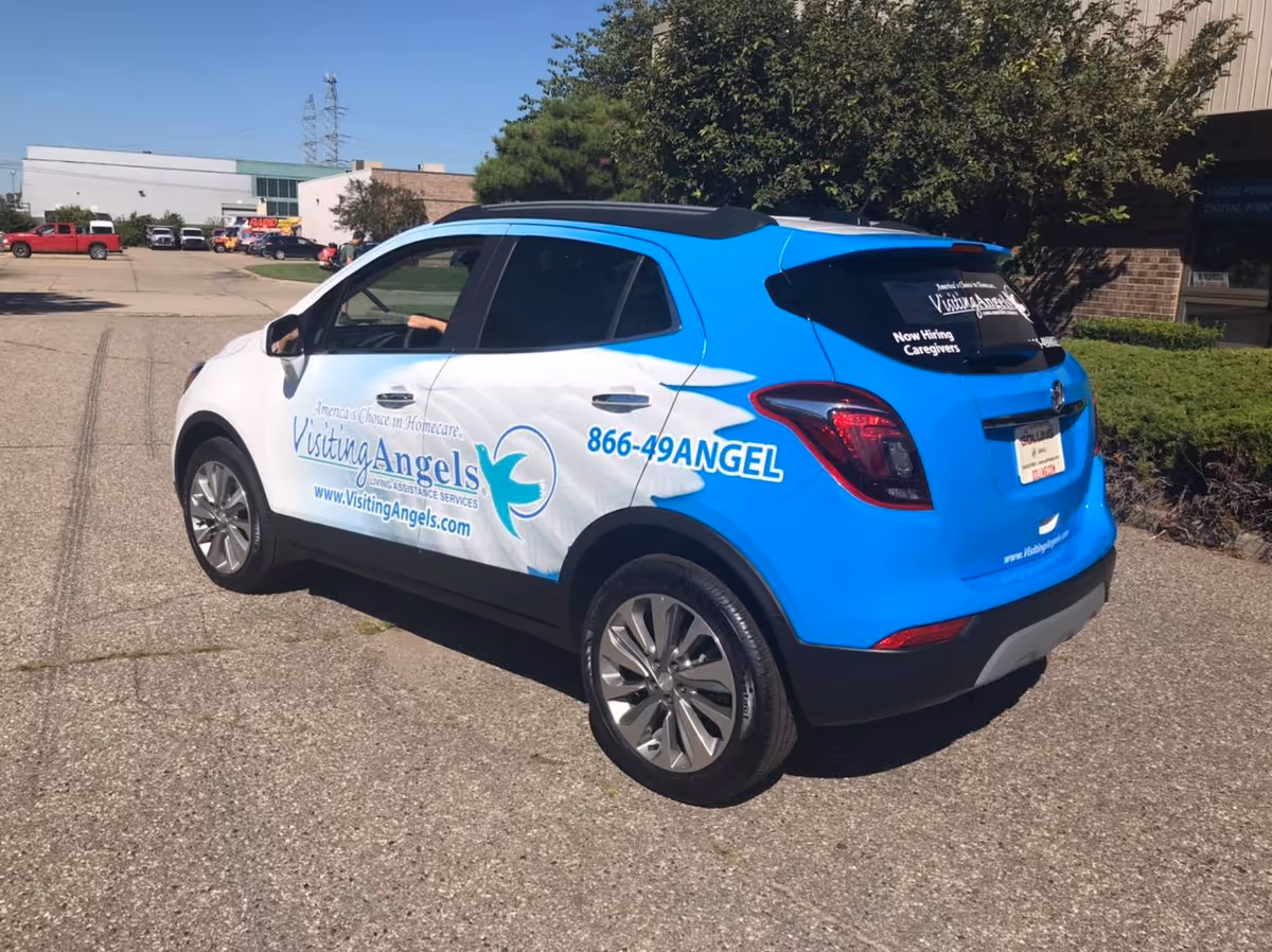 A blue-and-white Visiting Angels home care vehicle parked in a paved lot near a building.
