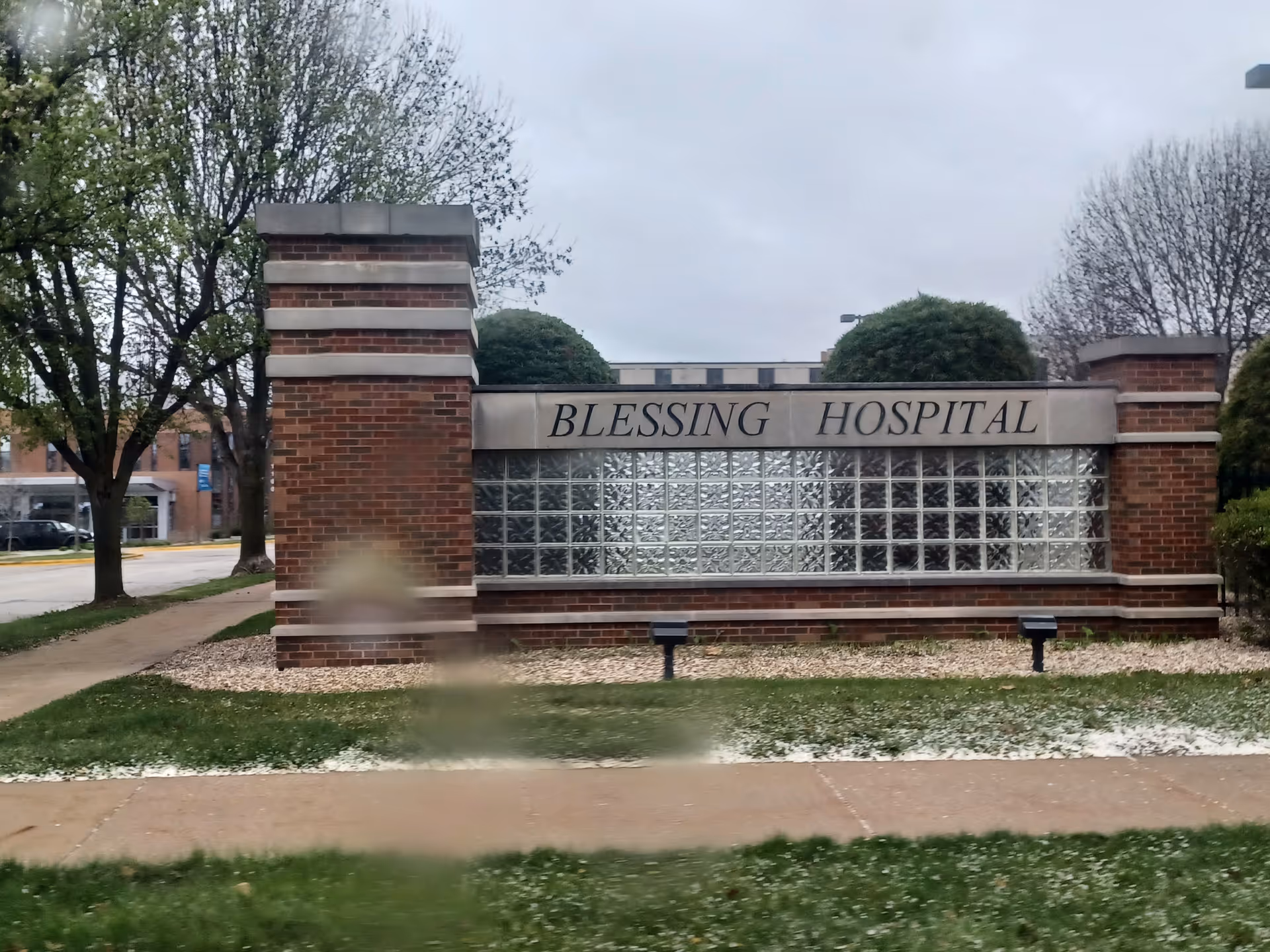 Exterior brick sign reading Blessing Hospital with glass block wall and surrounding trees.