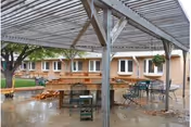 Outdoor covered patio with tables, chairs, and wooden benches in a courtyard.