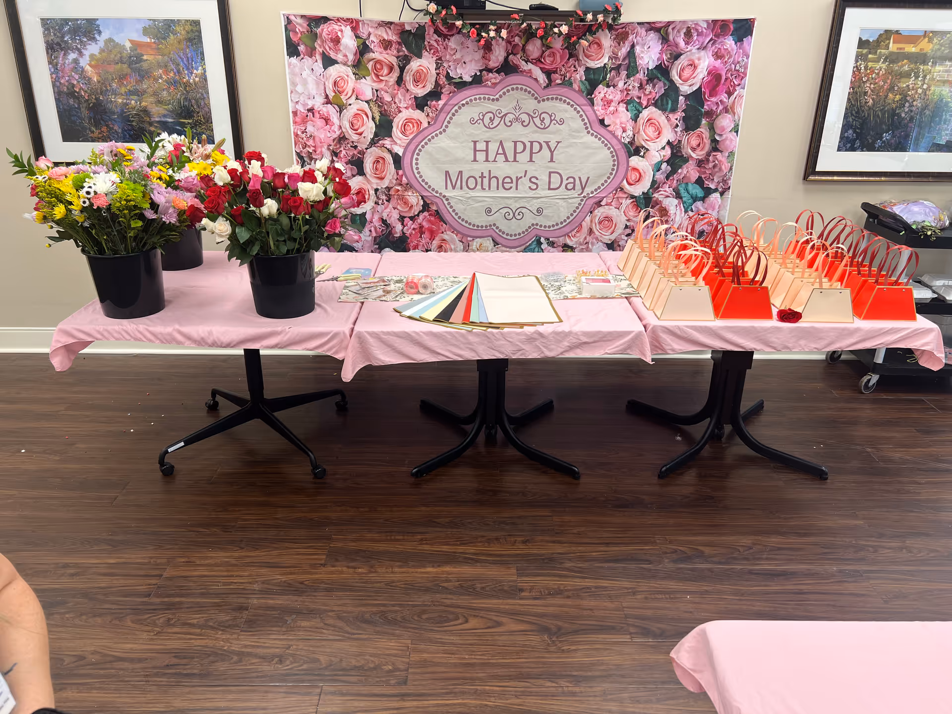 Interior event table setup with pink tablecloths, flowers, and Mother's Day backdrop.