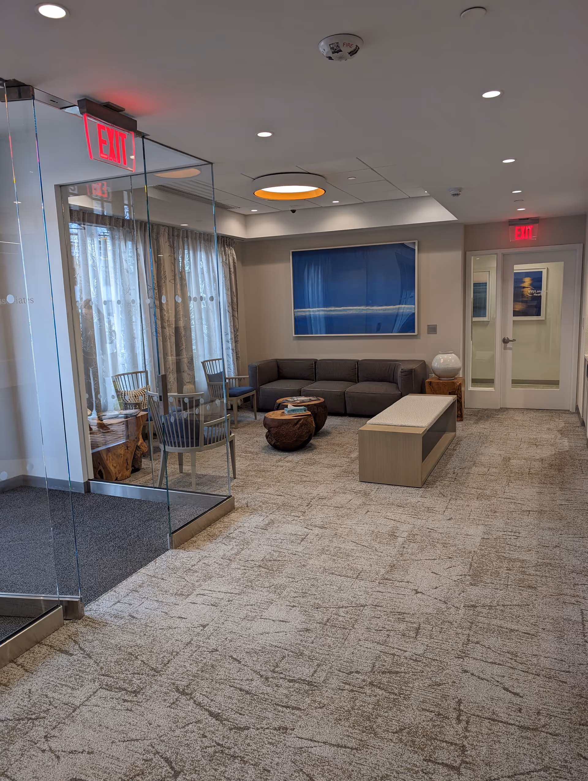 Modern lounge area inside a senior facility with gray sectional, glass walls, and seating.
