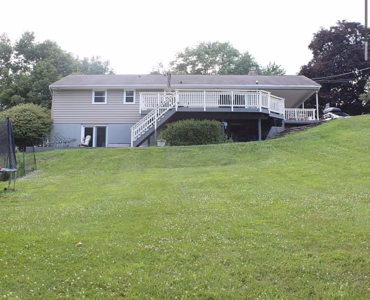 Slightly elevated house with a wooden deck, stairs, and expansive green lawn.