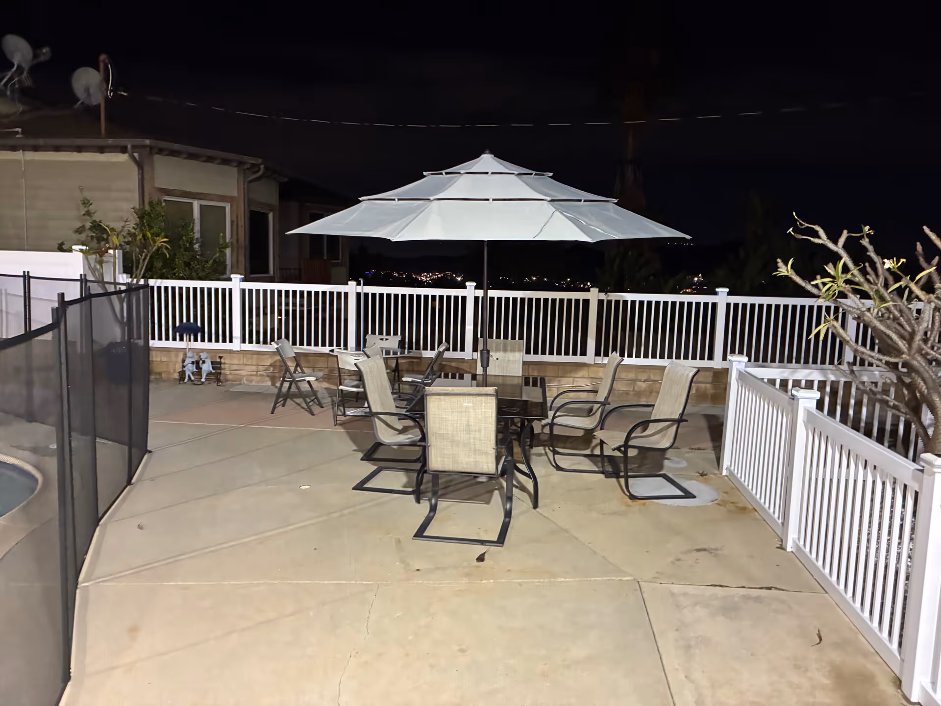 Nighttime outdoor patio with table, chairs, and a large umbrella surrounded by white railing.
