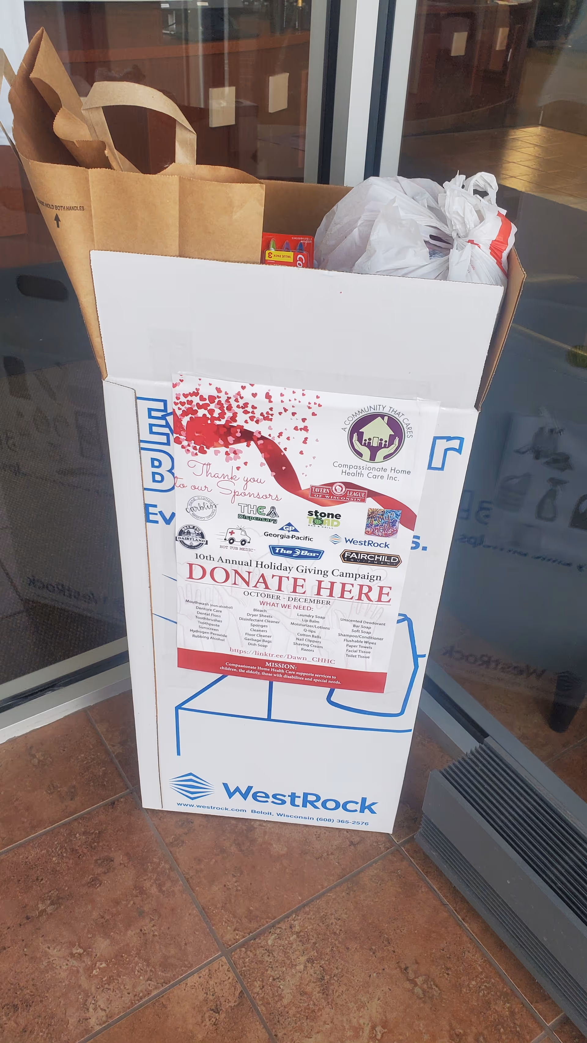 Donation box outside Compassionate Home Health Care INC with bags and flyers.