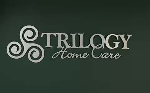 Sign reading Trilogy Home Care with a decorative emblem on a dark green wall.
