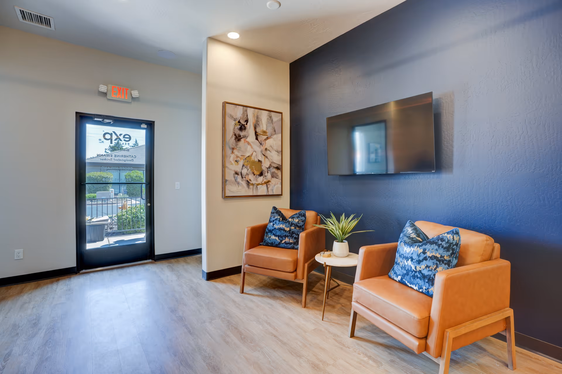 Two orange armchairs with blue pillows sit by a small table and mounted TV.
