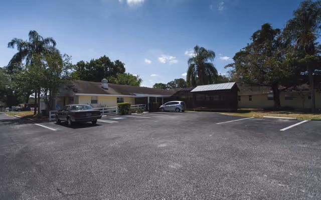 Front exterior of a single-story senior living facility with parking and trees.