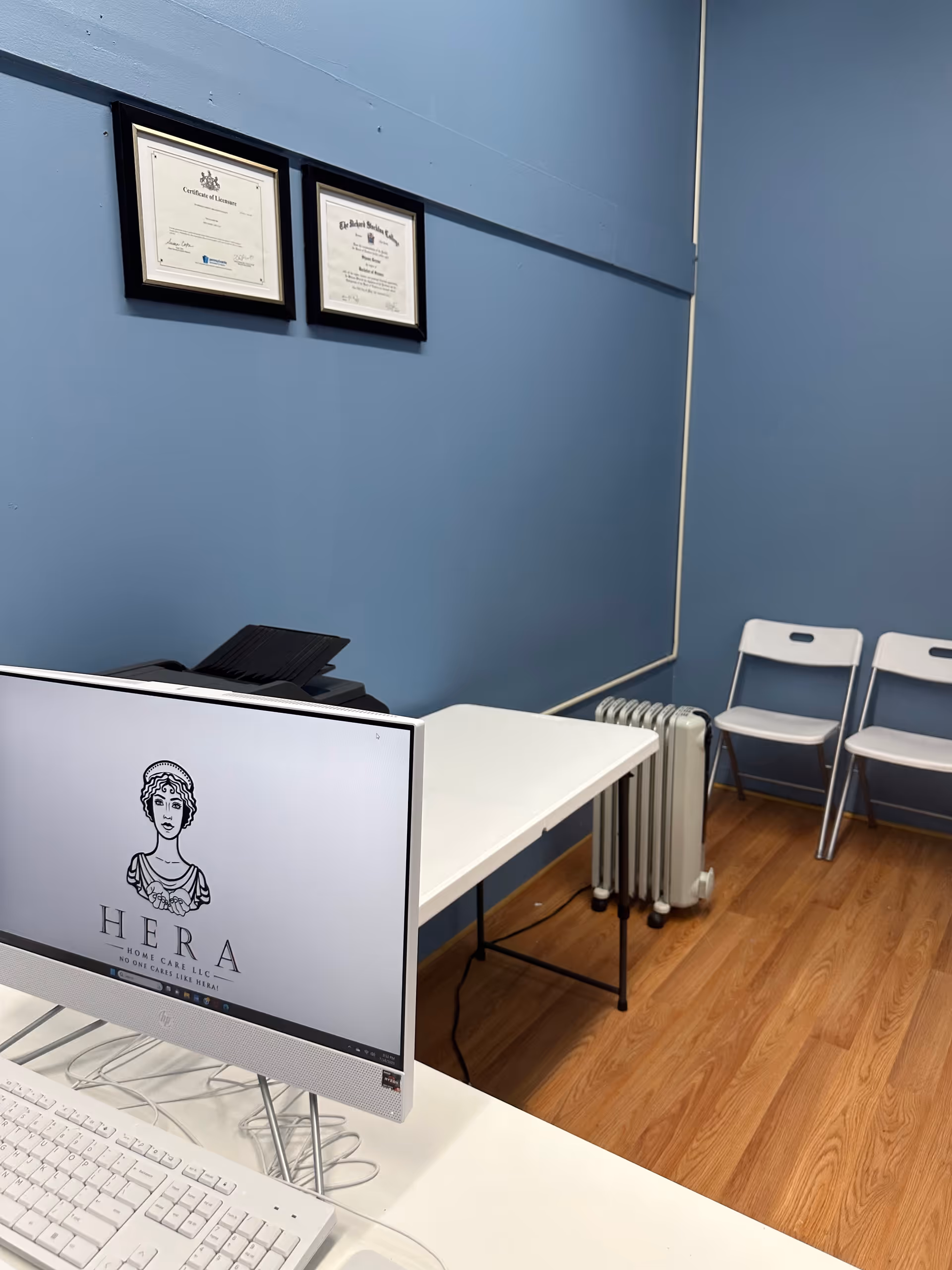 Blue-walled office area with framed certificates, a desk, and a Hera monitor.