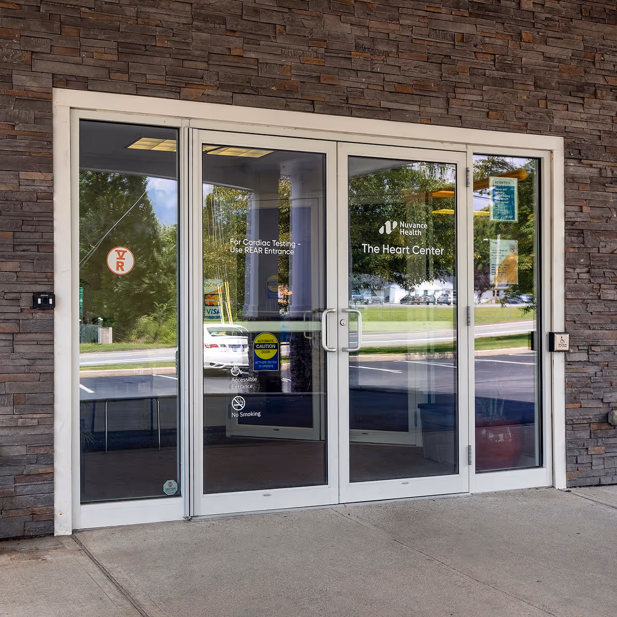 Glass automatic doors with Nuvance Health The Heart Center sign on a stone exterior wall.