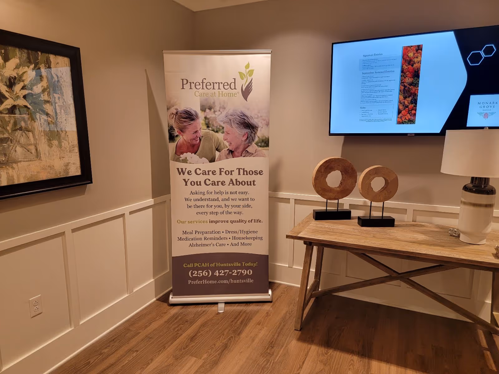 Indoor lobby with a Preferred Care at Home banner, wall art, and a wooden table.