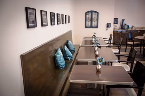 Row of dining tables with chairs and teal cushions in a cozy dining area.