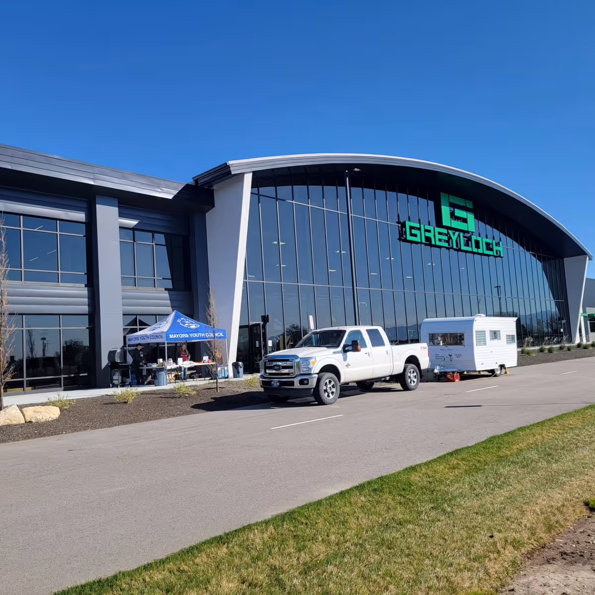 Modern glass-front building with curved roof, a white pickup, and a trailer in front.