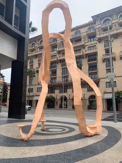 A large peach-colored abstract sculpture in an urban outdoor plaza.