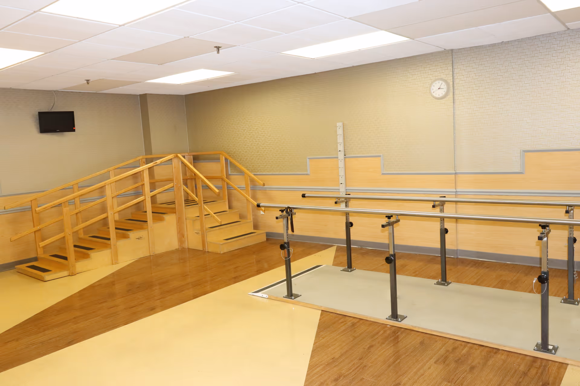 Indoor rehabilitation gym with parallel bars, wooden steps, and railing in a senior facility.