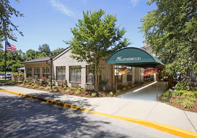 Exterior view of Heatherwood Retirement Community with entrance canopy, landscaping, and flag.
