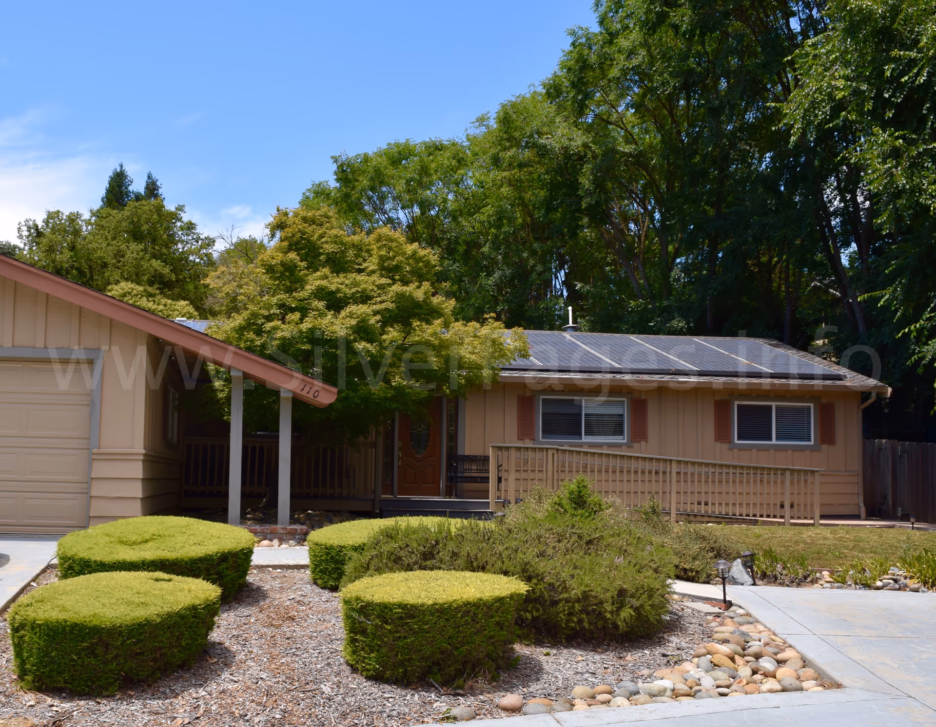 A single-story beige senior residence with a front porch, solar roof, and manicured shrubs.