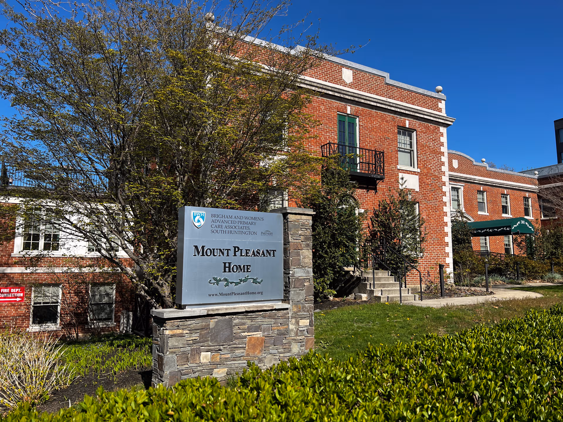 Exterior view of Mount Pleasant Home brick building with front sign and greenery.