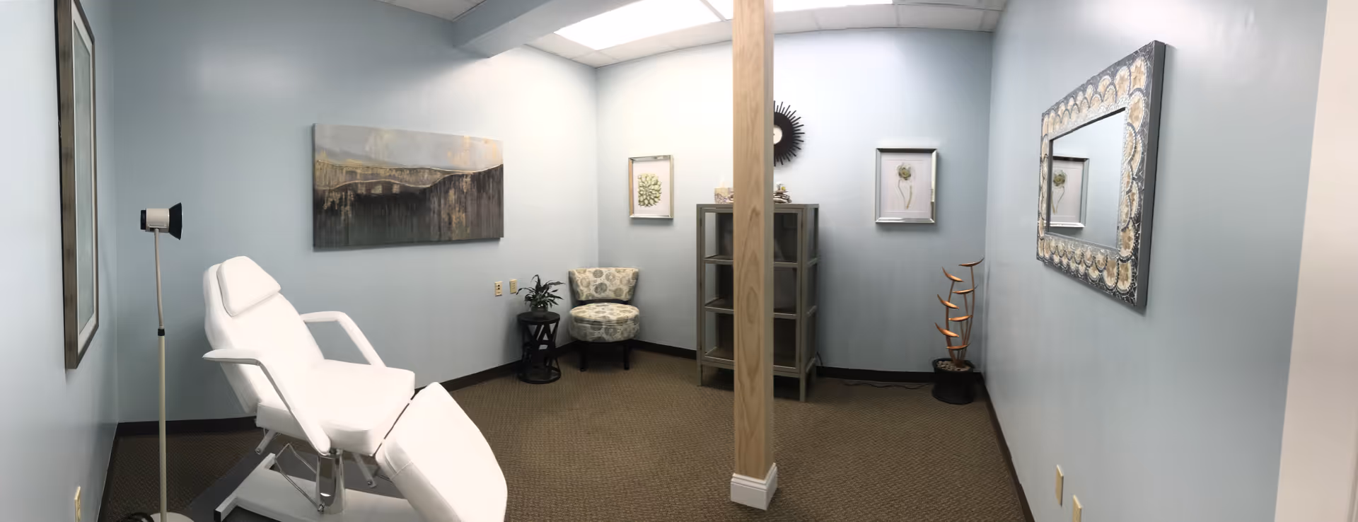 Blue-walled interior room with a white reclining chair, artwork, and a central pillar.
