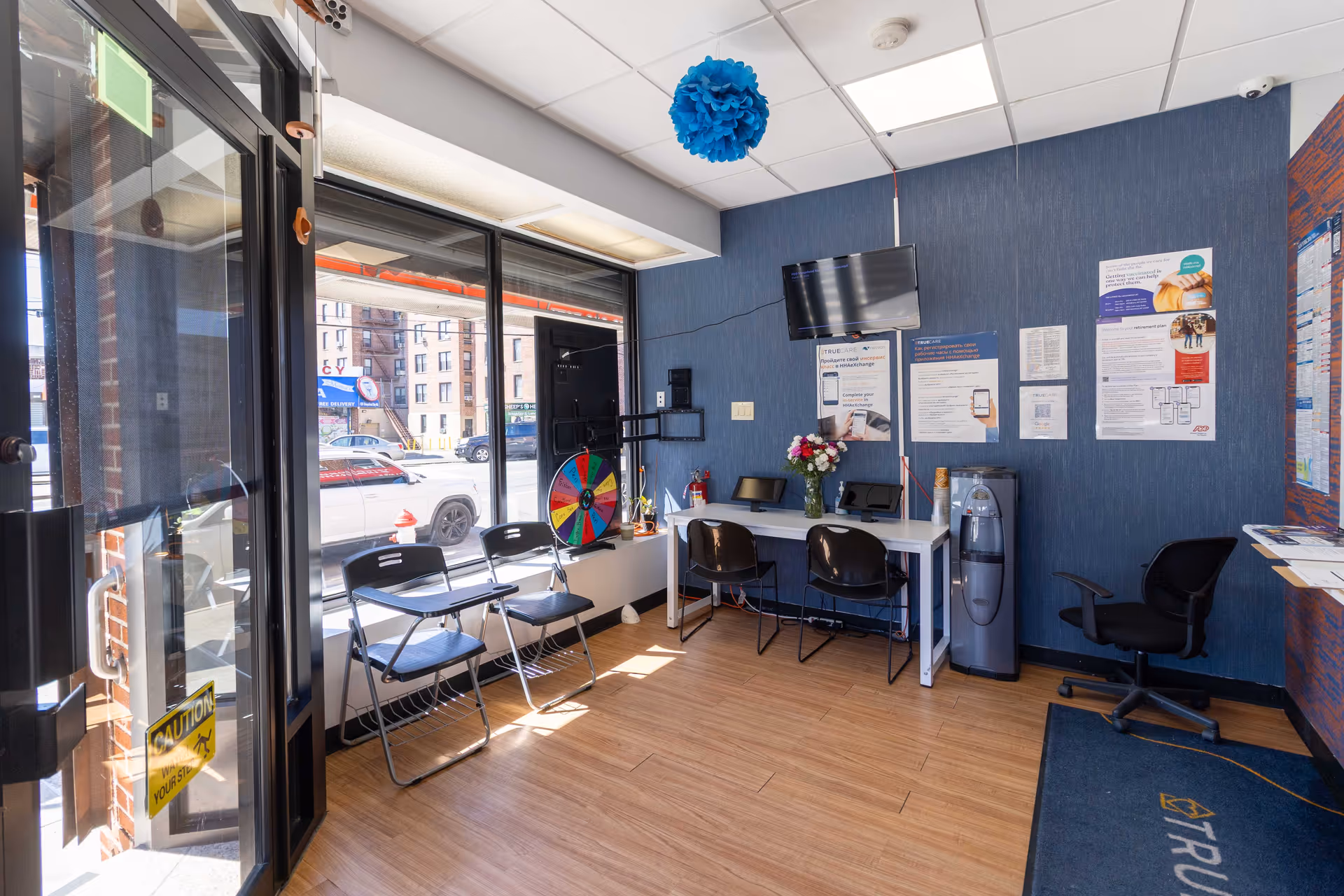 Bright interior reception area with blue walls, chairs, a desk, posters, and a TV.