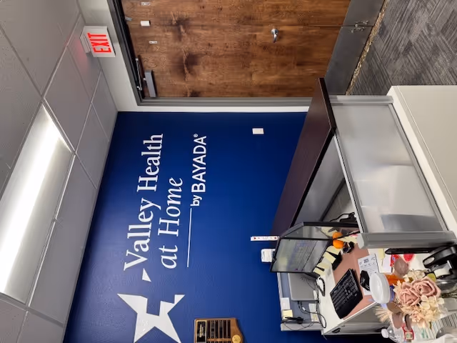 Blue wall signage reads 'Valley Health at Home by BAYADA' beside a desk.
