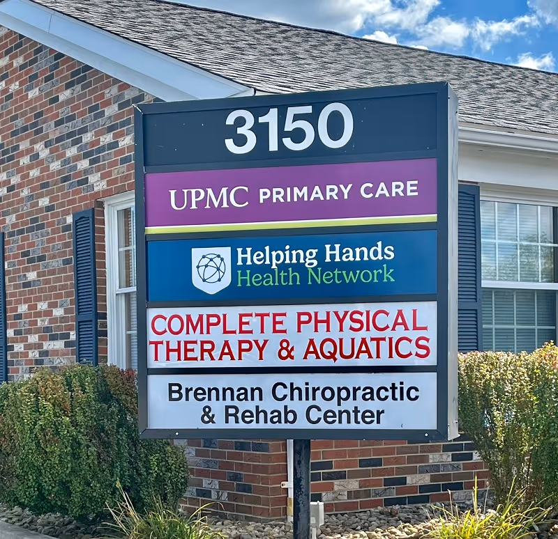 Exterior sign on brick building lists several healthcare providers including Helping Hands Health Network