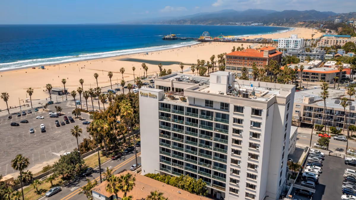 Tall white oceanfront building with a parking lot and sandy beach nearby.