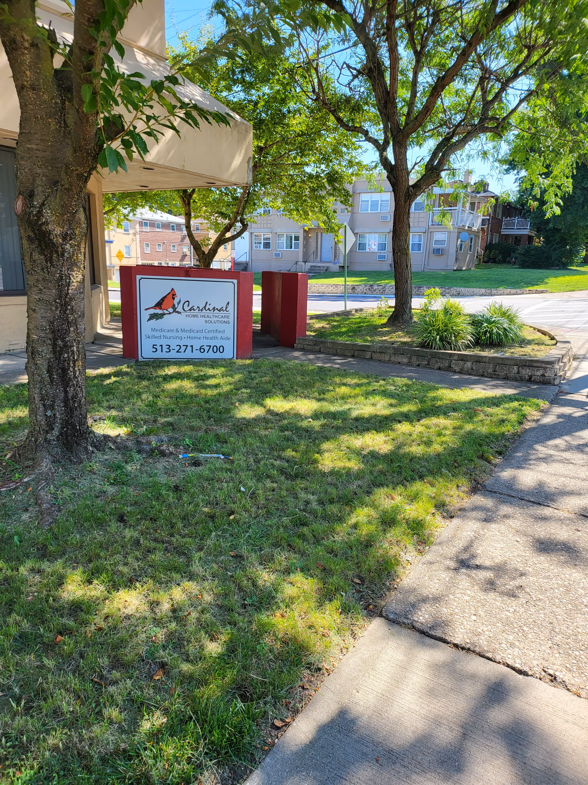 Exterior scene with Cardinal Home Healthcare Solutions sign beside trees and a sidewalk.