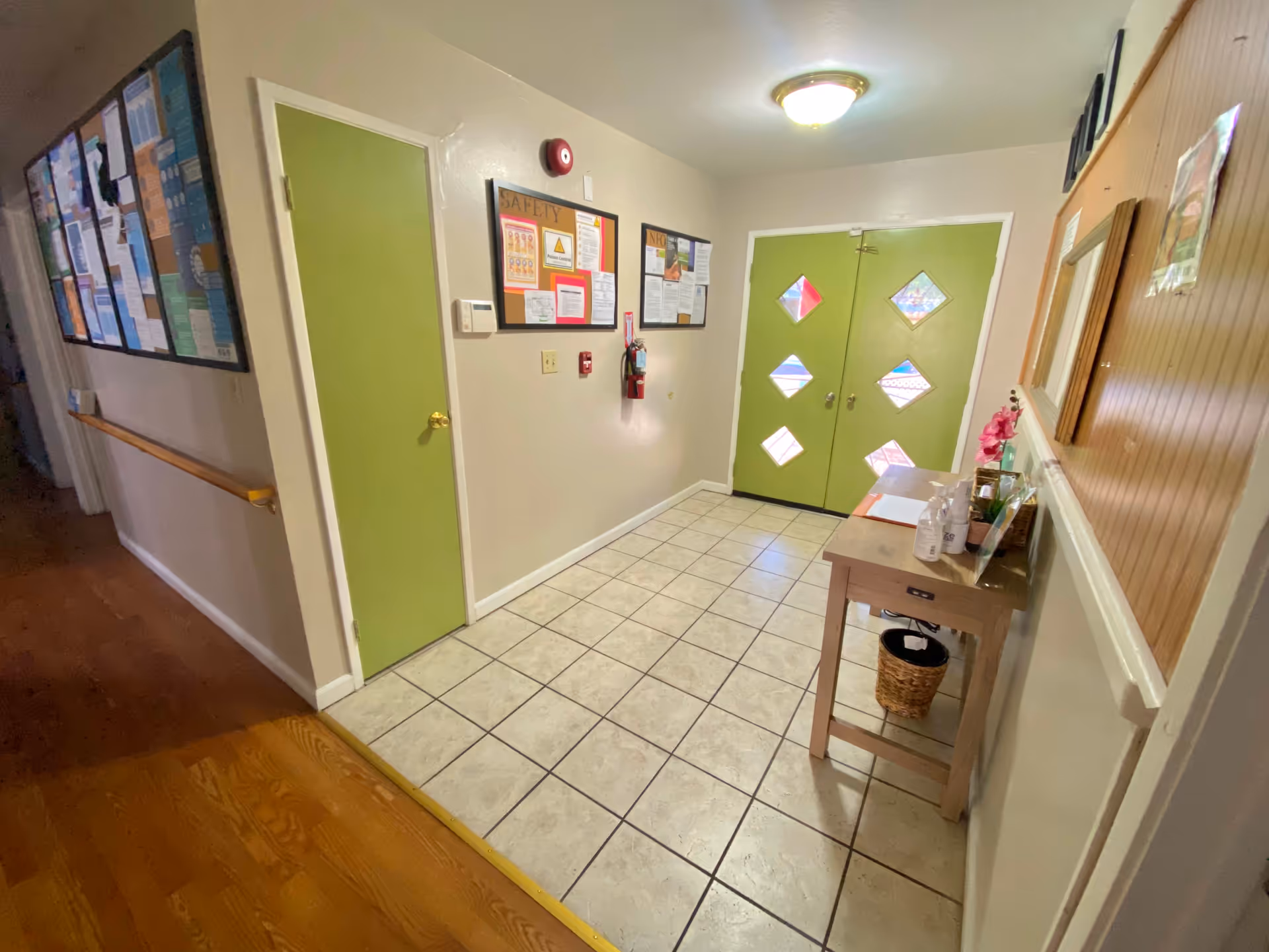 Interior hallway with green doors, bulletin boards, and a small table near the wall.
