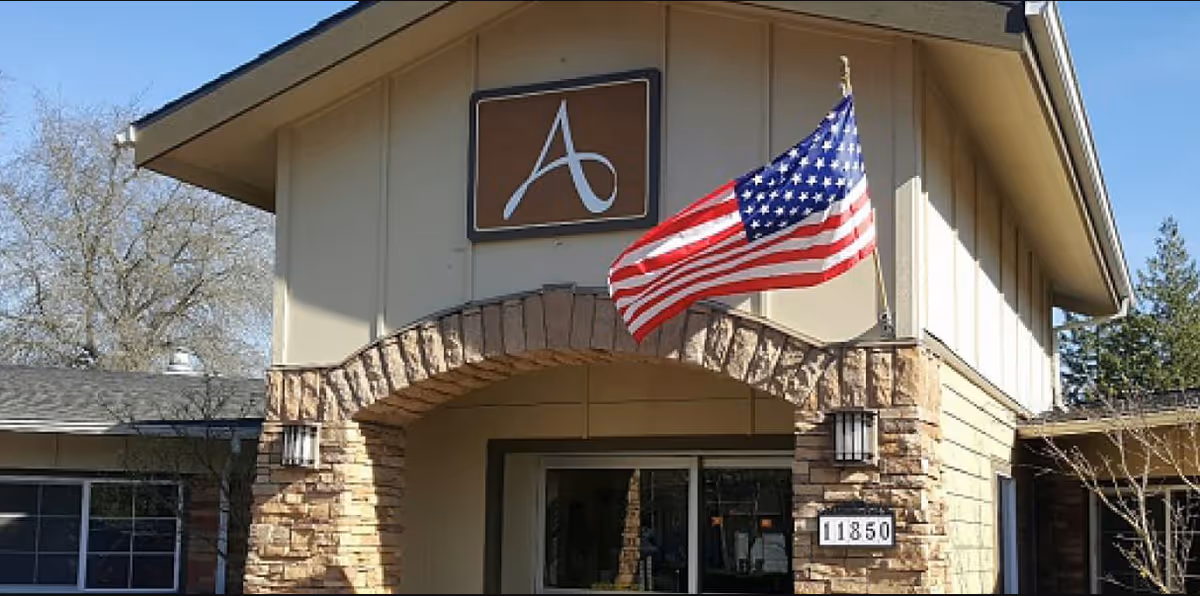 Entrance of Avamere Rehabilitation Beaverton facility with stone arch and waving American flag.