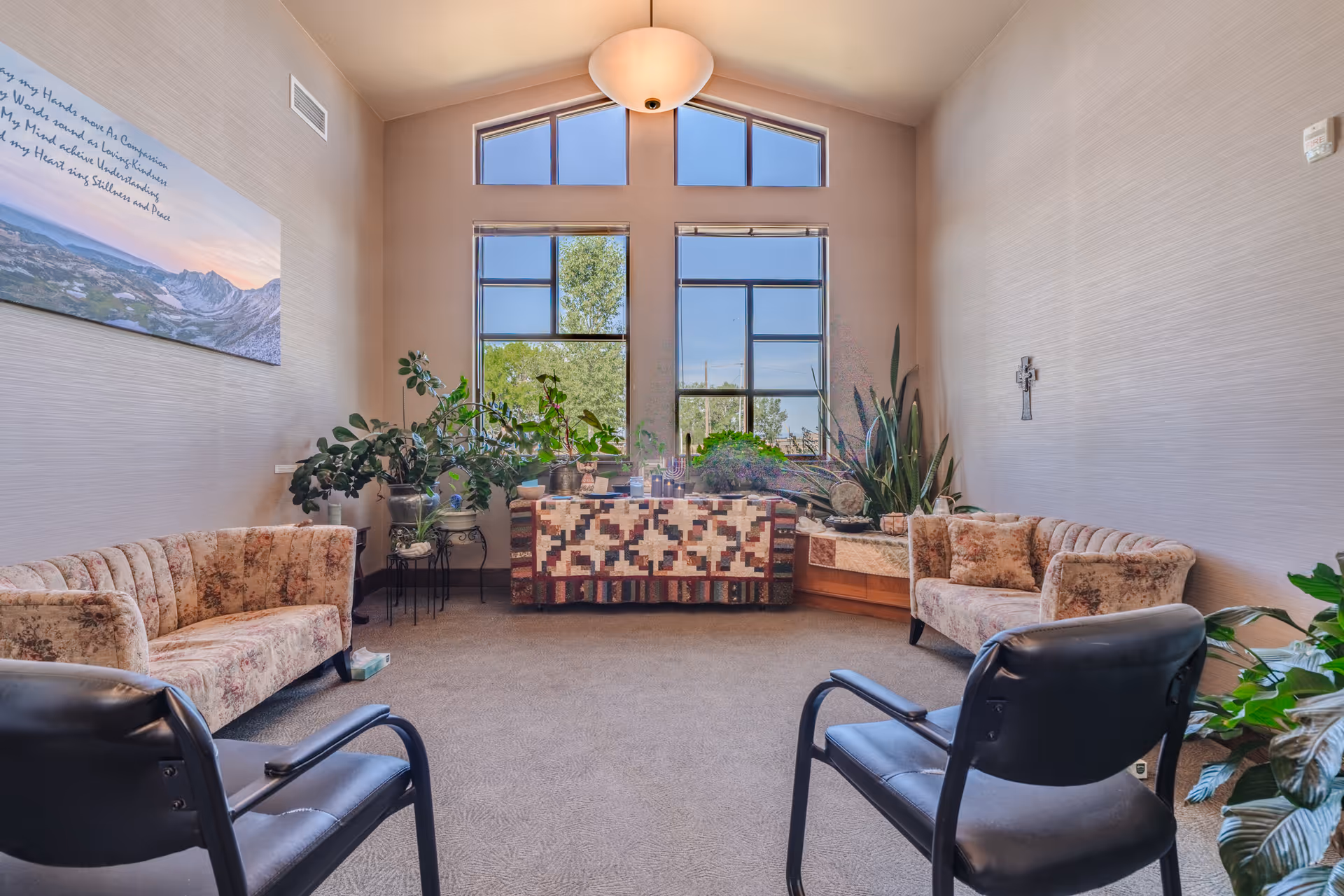 A bright hospice lounge with seating, plants, and a large window wall.