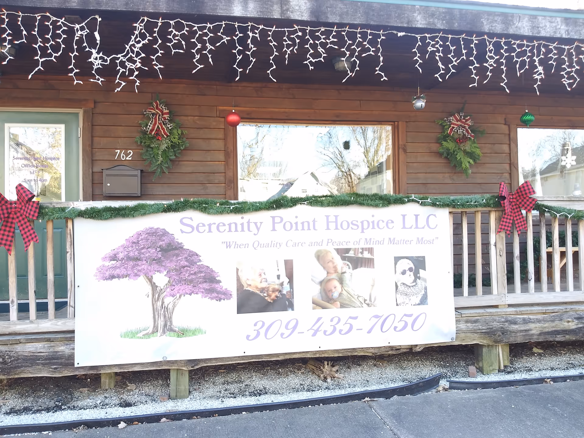 Wooden building front with a porch banner for Serenity Point Hospice and holiday lights.
