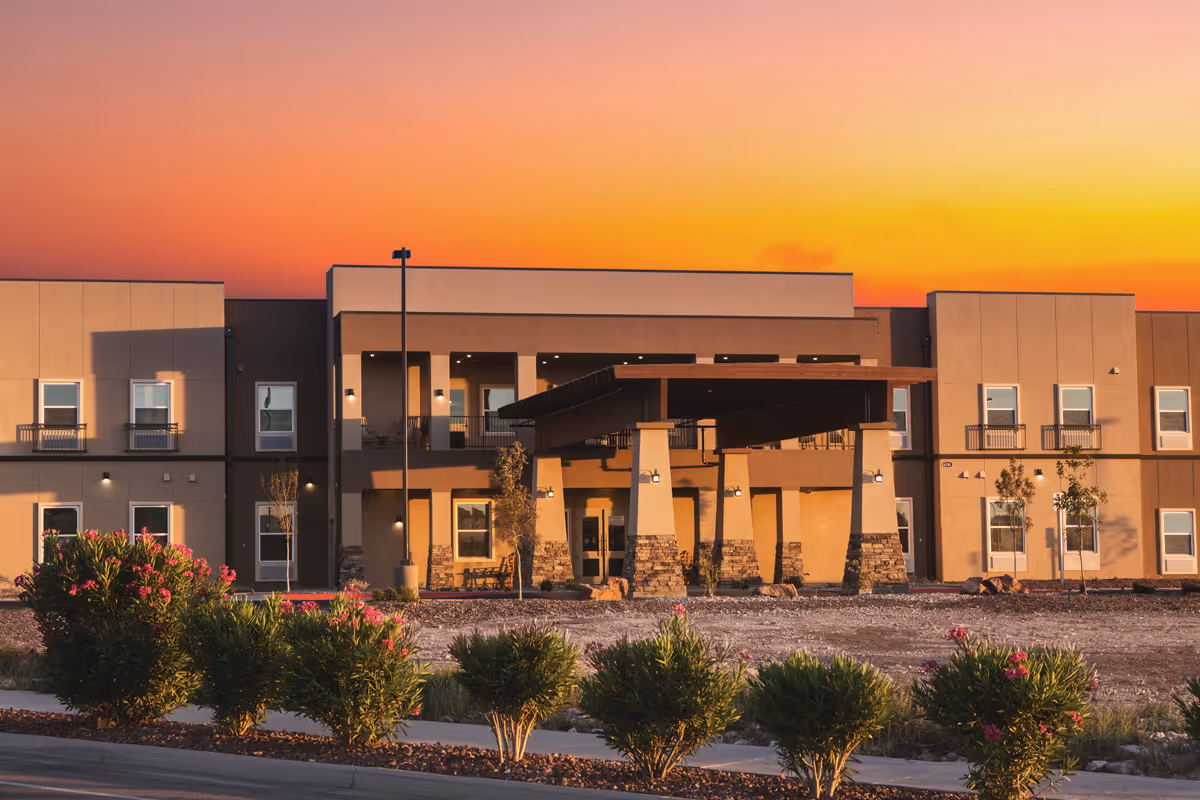 Sunset-lit exterior facade of The Legacy at Cimarron with entrance and desert landscaping.