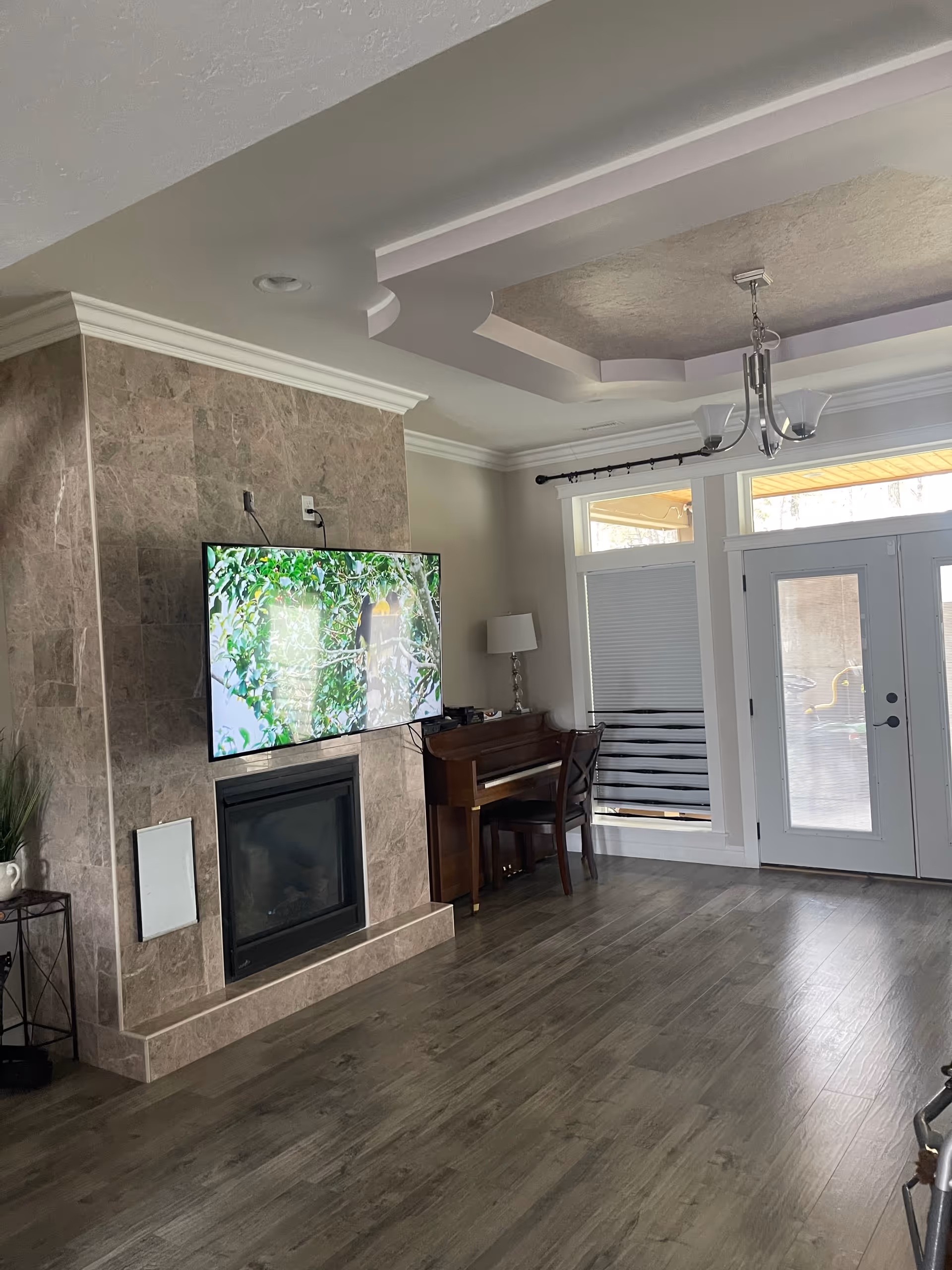 Living room at Harmony Lifecare Adult Family Home featuring fireplace, TV, piano, and glass doors.
