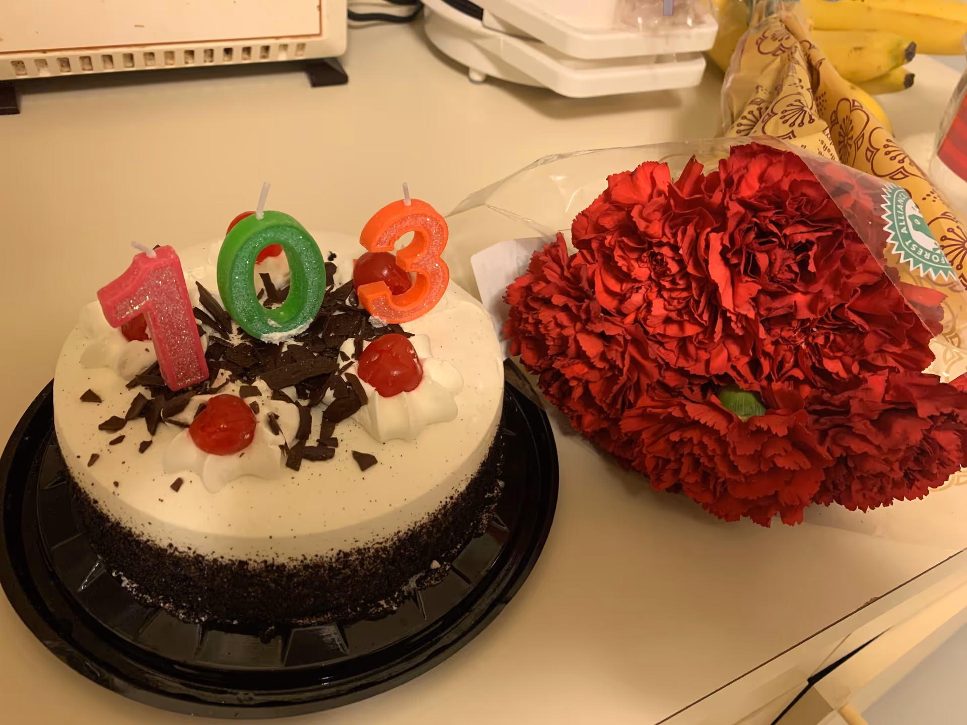 Birthday cake with candles and a red bouquet on a kitchen counter.