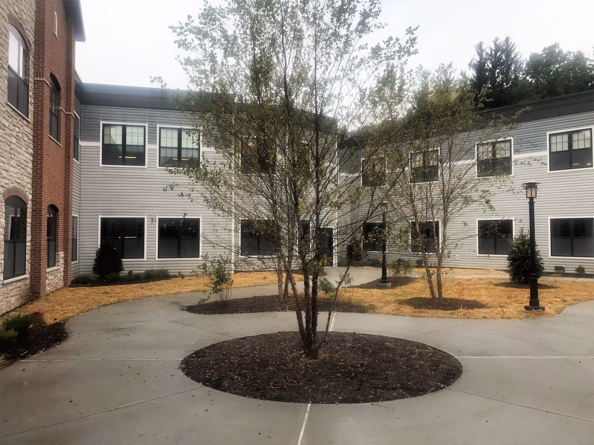 Two-story facility with gray siding, courtyard trees, and lampposts.