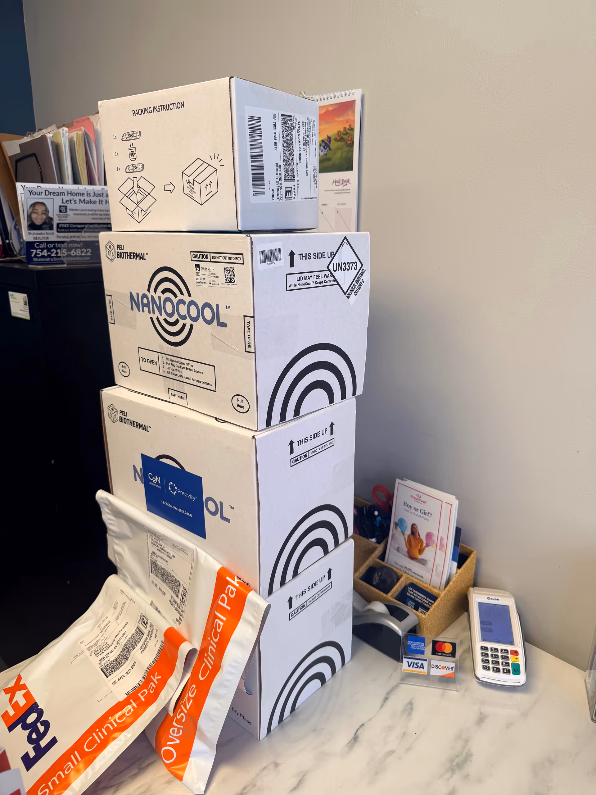Stacked Nanocool boxes, a card reader, and brochures on a marble countertop.