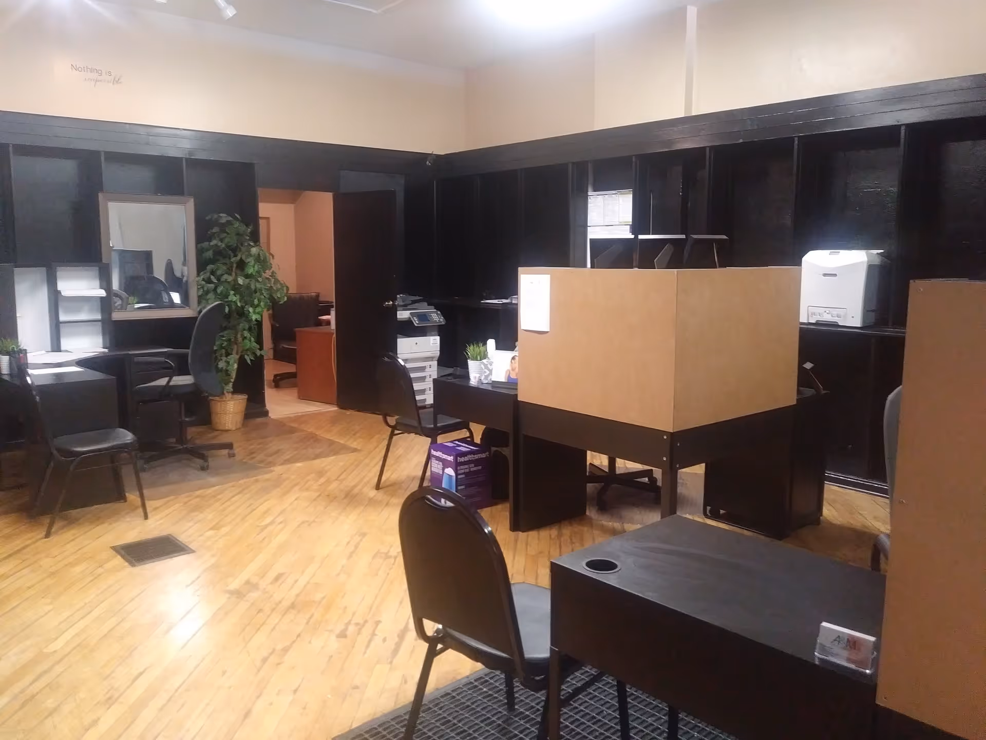 An office area with cubicles, desks, chairs, and dark partition panels.