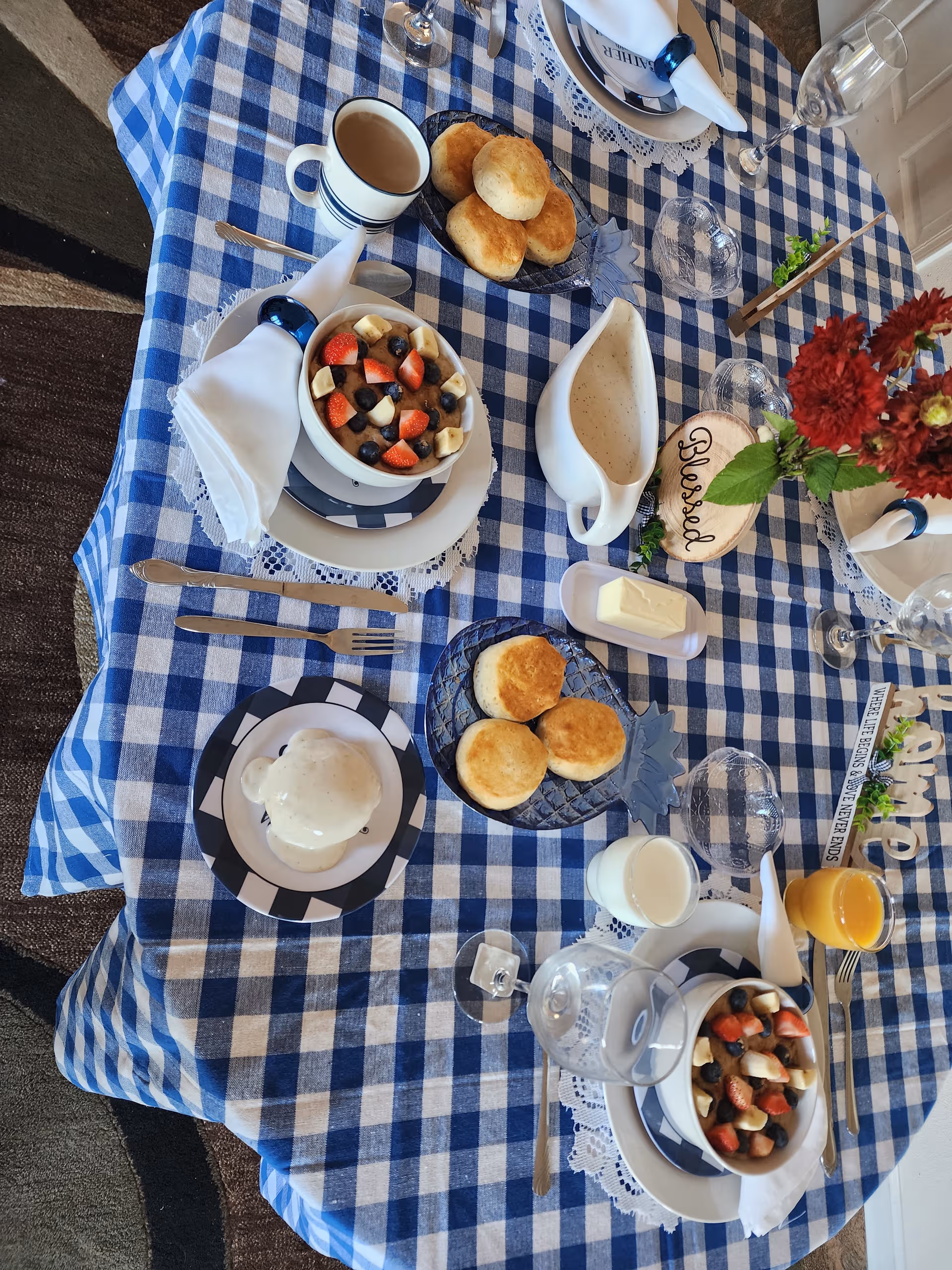 Dining table set for a meal with fruit bowls, scones, cream, and flowers.