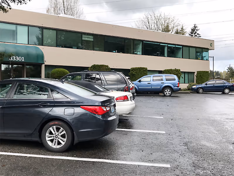 Exterior view of a two-story building with a green awning and parked cars.