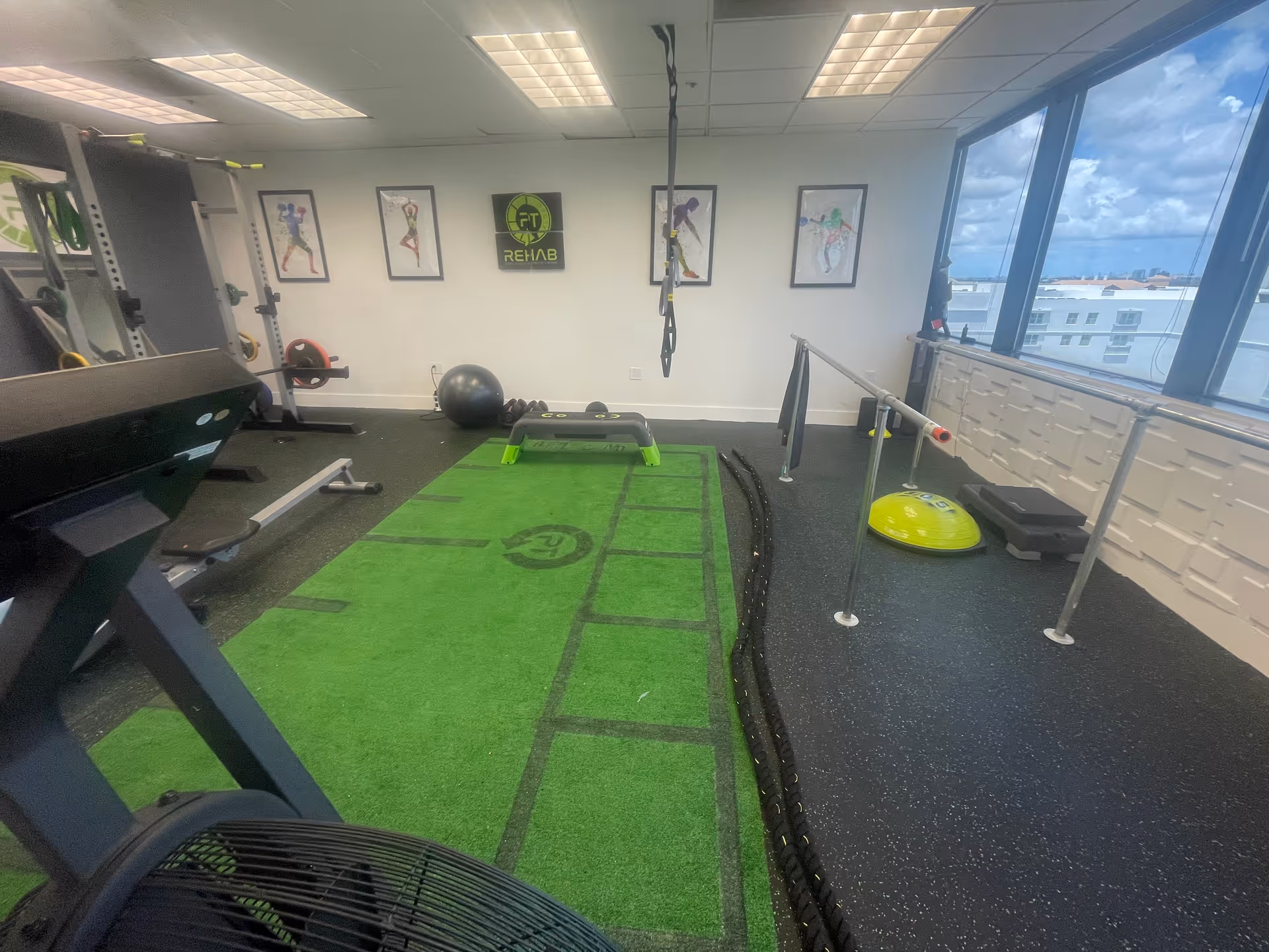 Indoor gym at Reload Physical Therapy with turf mat, equipment, and large windows.