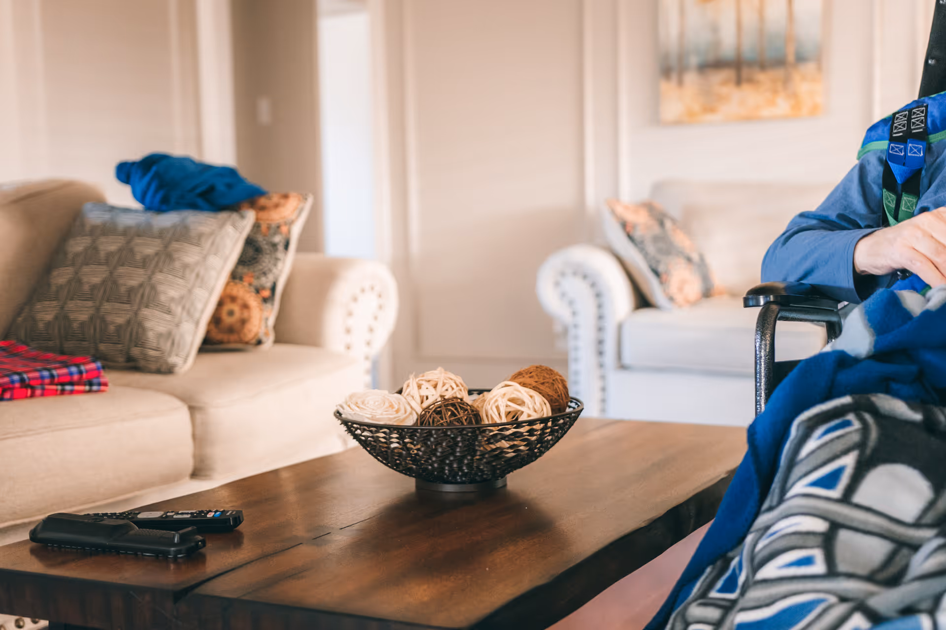 Cozy living room with beige couches, pillows, a coffee table, and a resident partially visible.