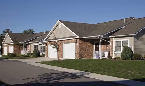 Exterior view of Elderwood Residences at Cheektowaga townhomes with garages and green lawn.