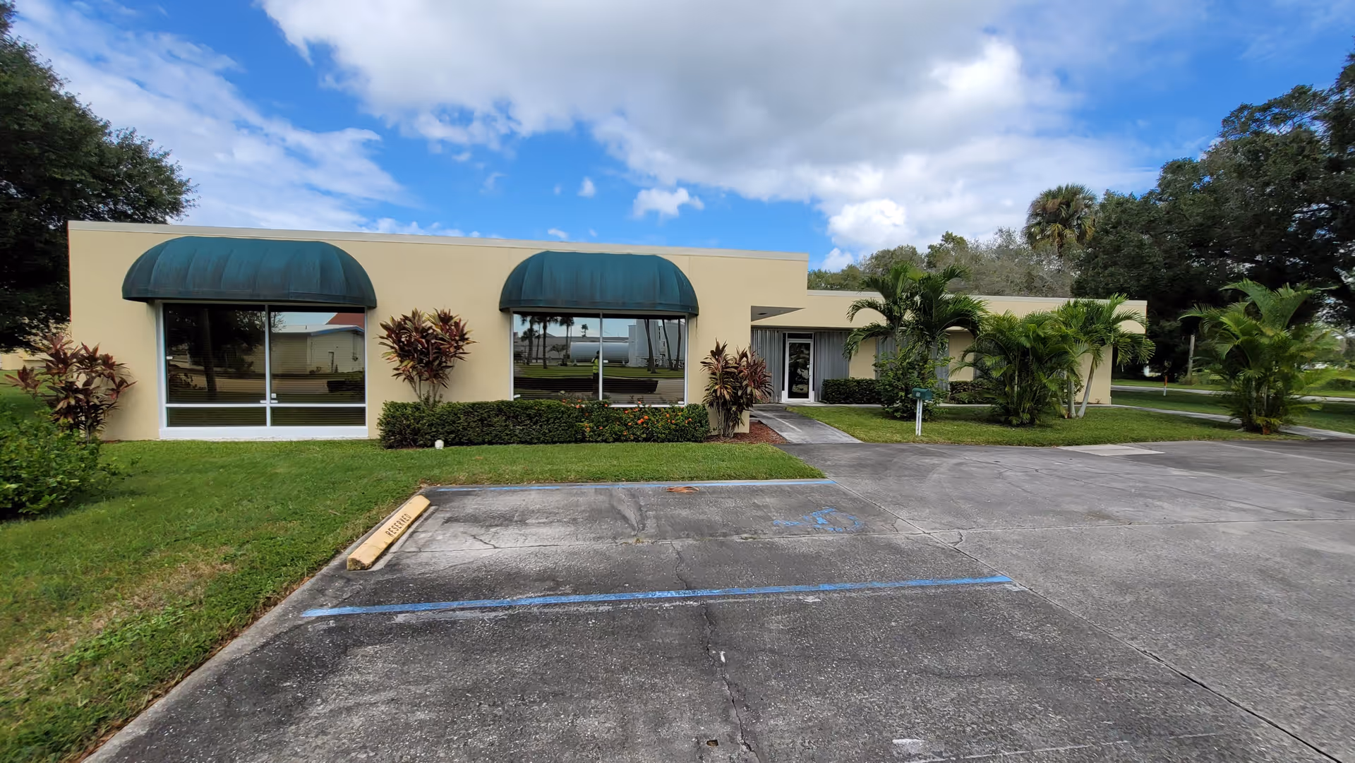 Exterior view of a beige senior living facility with green awnings and a parking lot.