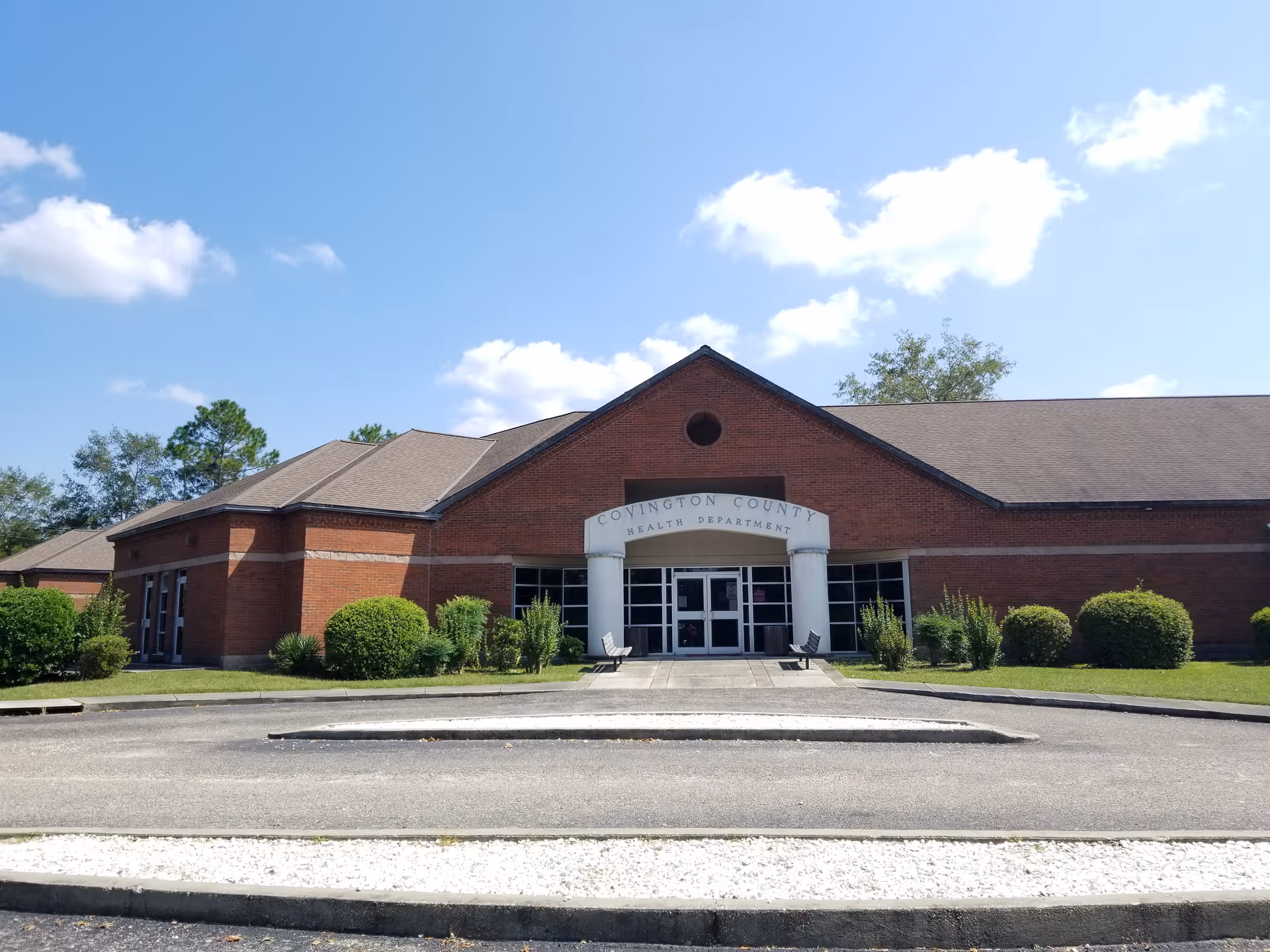 Brick Covington County Health Department building with glass doors and manicured shrubs.
