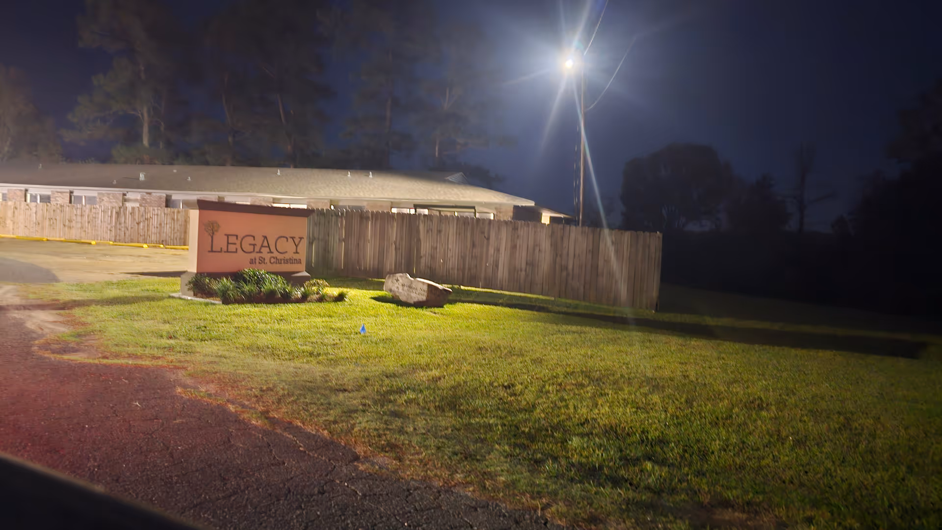 Night exterior view of the nursing facility sign beside a wooden fence.