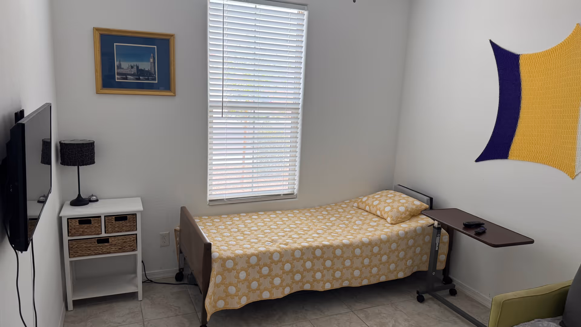 A small bedroom in a senior living facility with a single bed, nightstand, and desk.