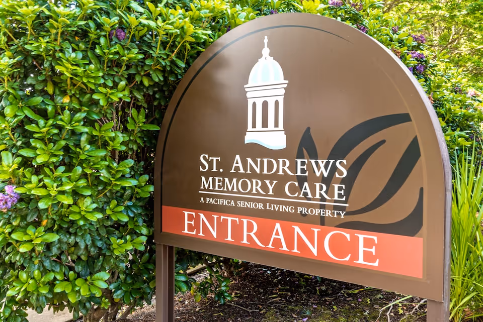 Outdoor entrance sign for St. Andrews Memory Care standing beside green shrubs.