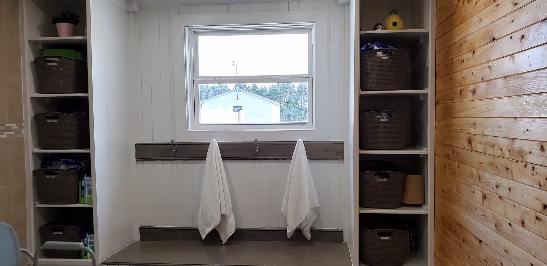 Two white towels hang from a rail between shelves of baskets in a storage nook.