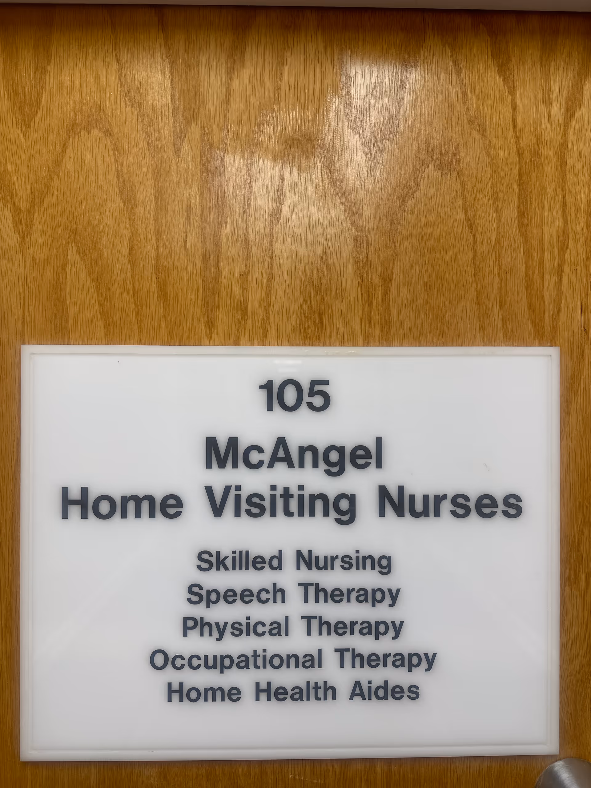 White sign on wooden door lists McAngel Home Visiting Nurses and services.