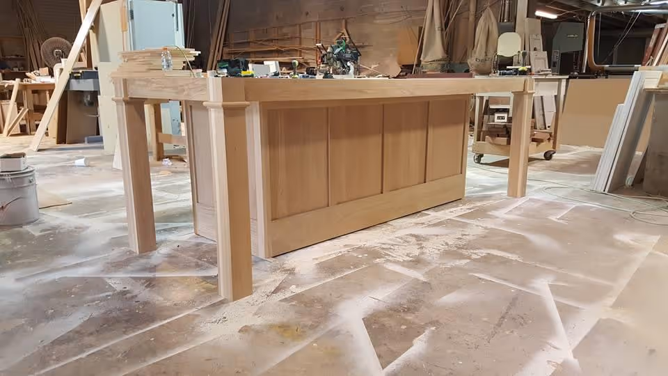 Wooden reception counter being built in a workshop with tools and wood panels.